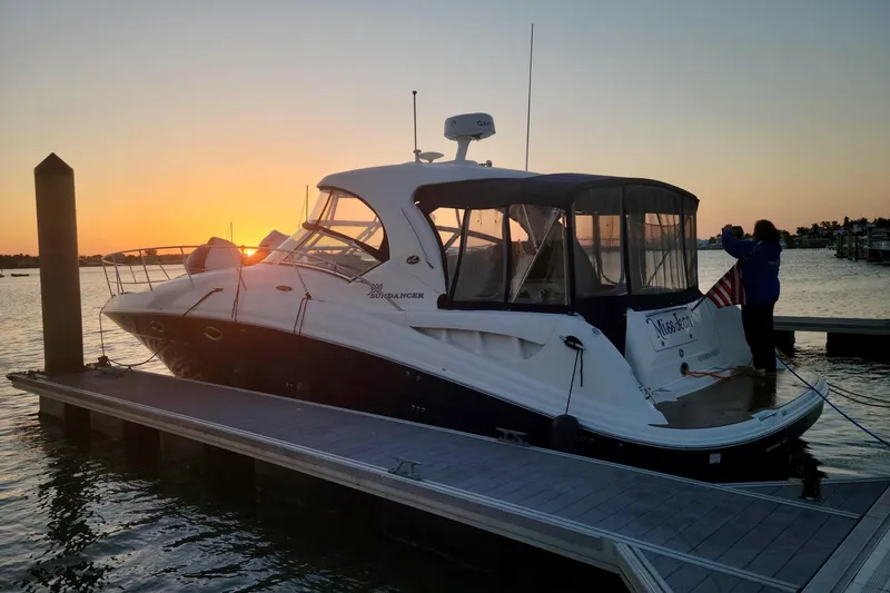 Slide: The Image of 2005 Sea Ray 390 Sundancer docked at sunset, with a person adjusting the flag. - 2