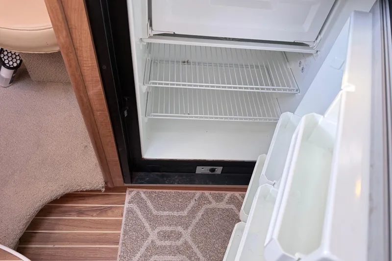 Slide: The Image of Open refrigerator inside 2002 Maxum 3100 SE boat, showing empty shelves and carpeted flooring. - 13