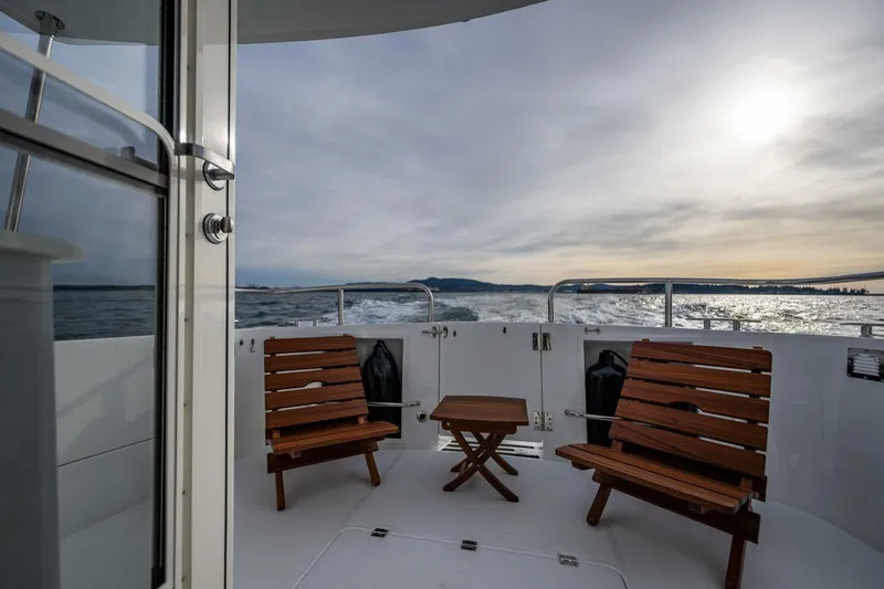 Slide: The Image of 2024 Nordic Tug 40 boat deck with wooden chairs, ocean view, and sunset. - 23