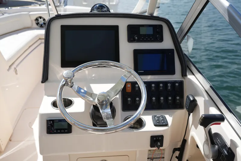 Slide: The Image of 2021 Grady-White Freedom 235 boat dashboard with steering wheel and electronic controls. - 29