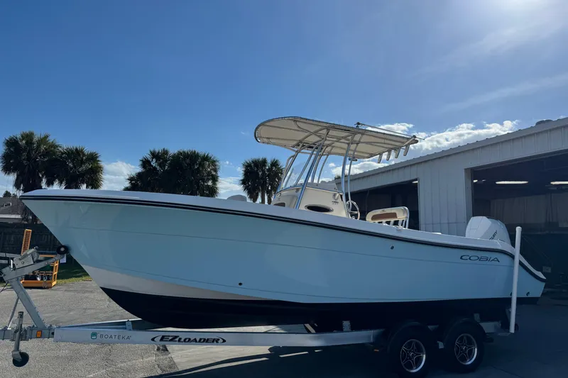 The Image of 2024 Cobia 237 Center Console boat on trailer, sunny day, palm trees in background. - 1