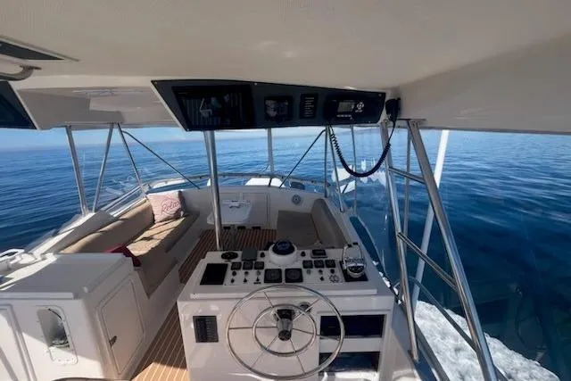 Slide: The Image of 1993 Riviera 47 Open Flybridge yacht interior with steering wheel and seating, on calm ocean waters. - 7