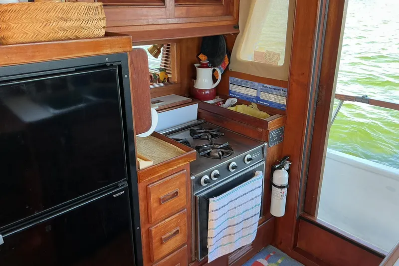Slide: The Image of 1977 Universal Marine Europa boat kitchen with stove, fridge, and wooden cabinetry. - 16