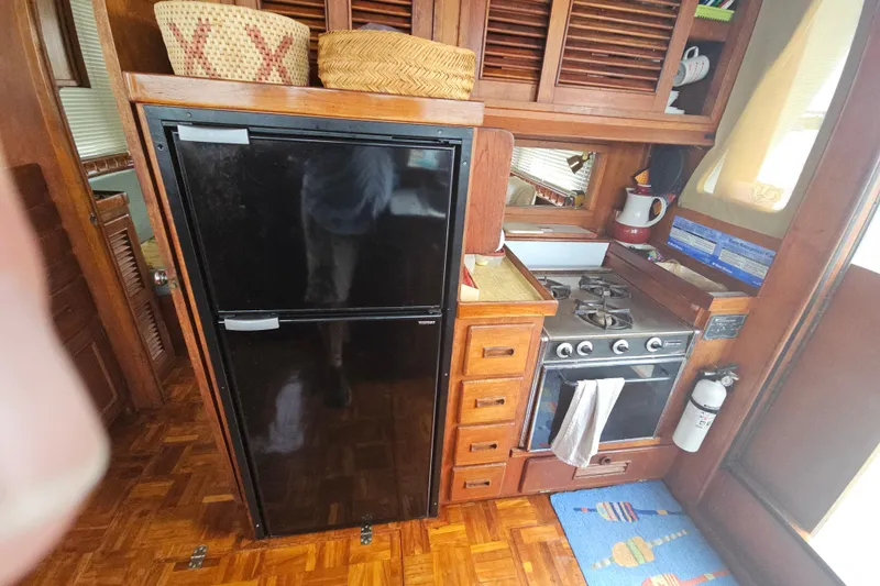 Slide: The Image of 1977 Universal Marine Europa yacht kitchen with stove, fridge, and wooden cabinetry. - 27