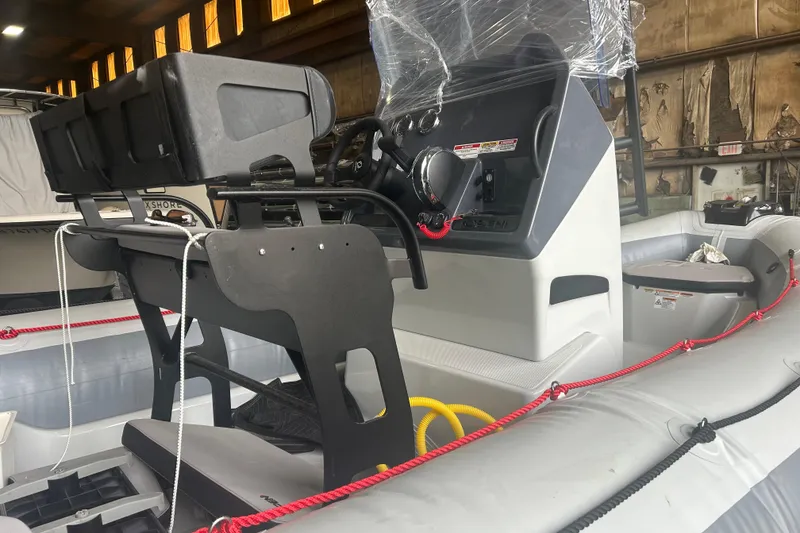 Slide: The Image of 2025 Zodiac Open 6.5 boat interior with steering console and seating in a warehouse. - 8
