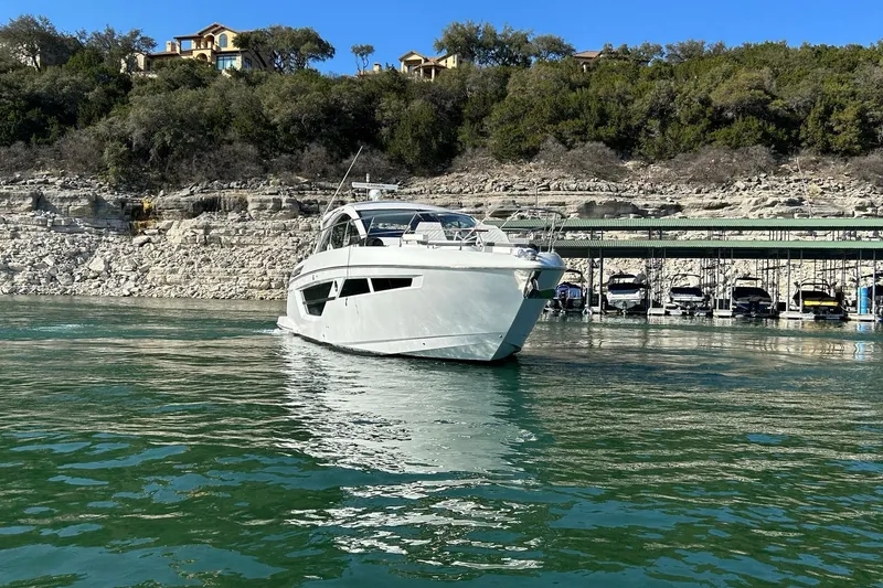 Slide: The Image of 2021 Cruisers Yachts 50 Cantius on serene lake with rocky shoreline backdrop. - 12