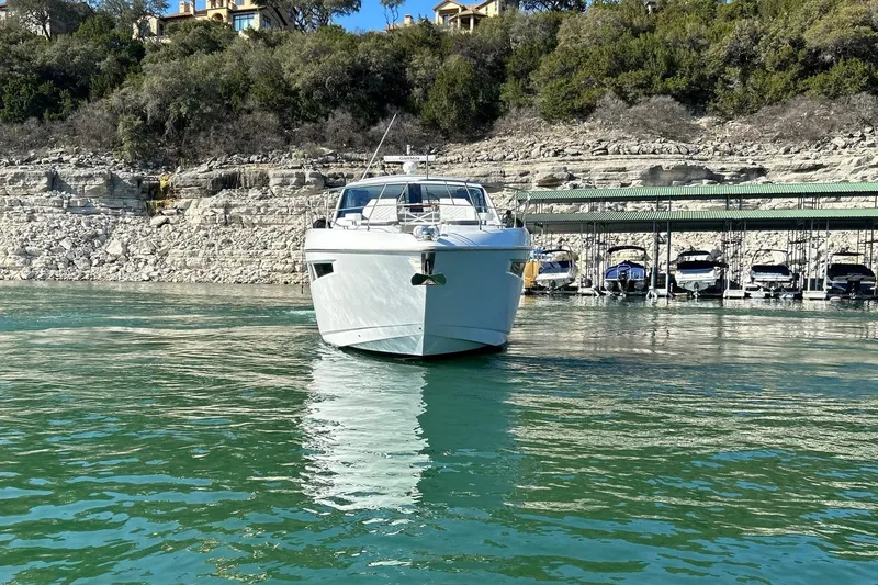 Slide: The Image of 2021 Cruisers Yachts 50 Cantius on serene water near rocky shoreline and docked boats. - 13