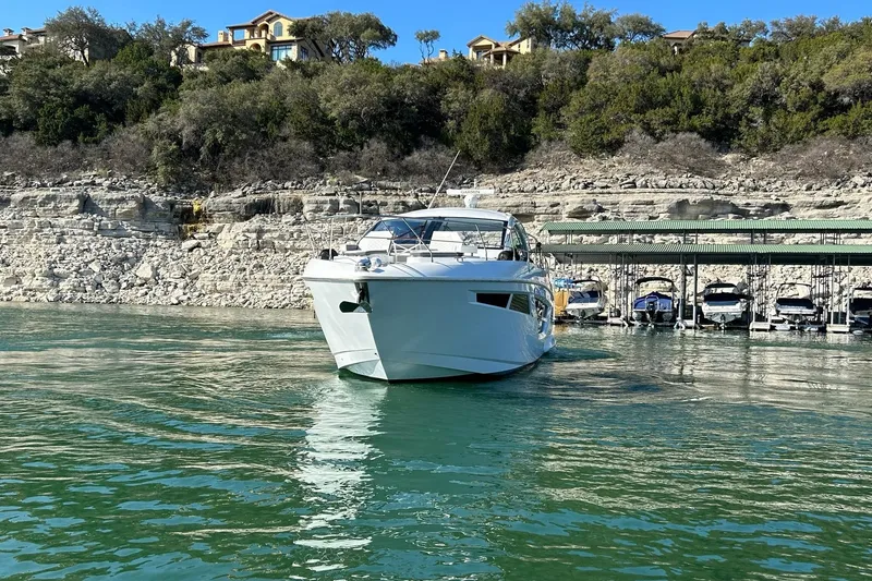 Slide: The Image of 2021 Cruisers Yachts 50 Cantius on serene lake near rocky shoreline and docked boats. - 14