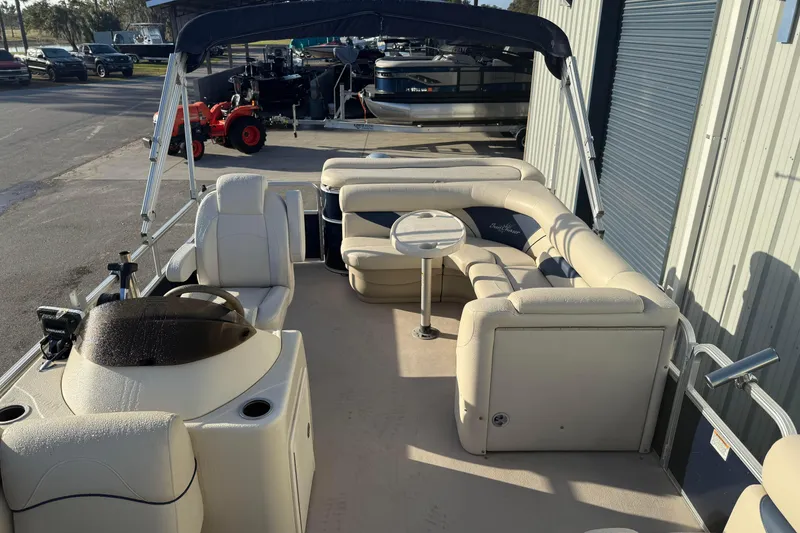 Slide: The Image of 2015 SunChaser 22 vs pontoon boat with beige seating and canopy, parked near a warehouse. - 13