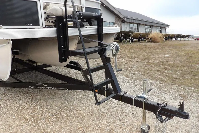 Slide: The Image of 2018 Bennington 23SF boat trailer with ladder, parked on gravel near a building. - 64