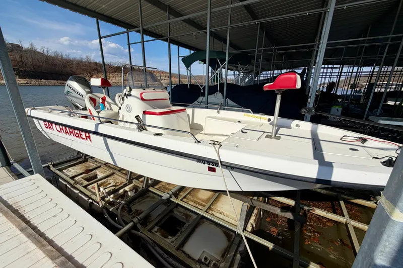 The Image of 2004 PlayCraft 22 Bay Charger boat docked, featuring red and white seating, under a covered marina. - 0