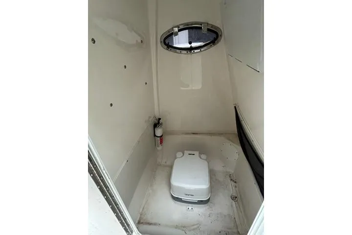 Slide: The Image of 2023 NauticStar 24 Legacy boat interior with portable toilet and porthole window. - 12