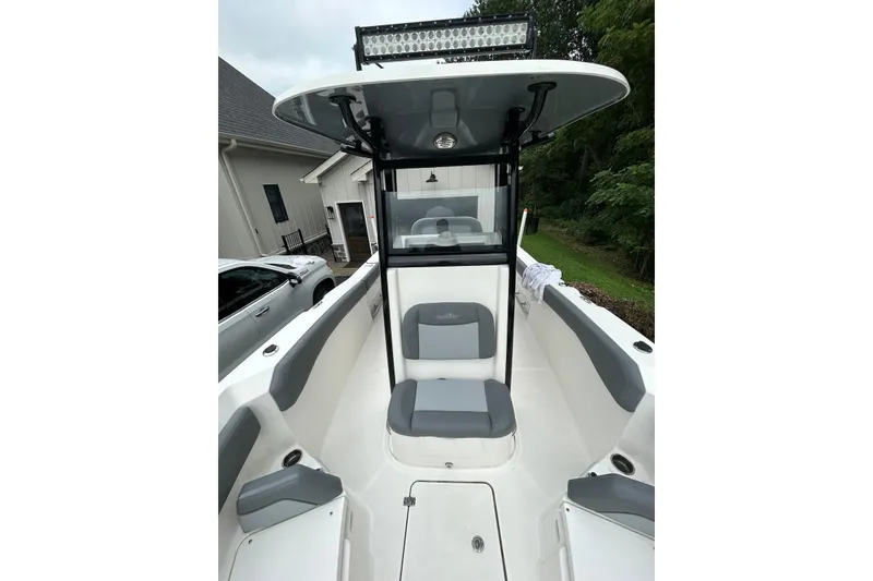 Slide: The Image of 2023 NauticStar 24 Legacy boat interior with seating and canopy, parked near a house. - 5
