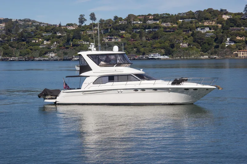 Slide: The Image of 1998 Sea Ray 480 Sedan Bridge yacht on calm water with scenic hillside background. - 2