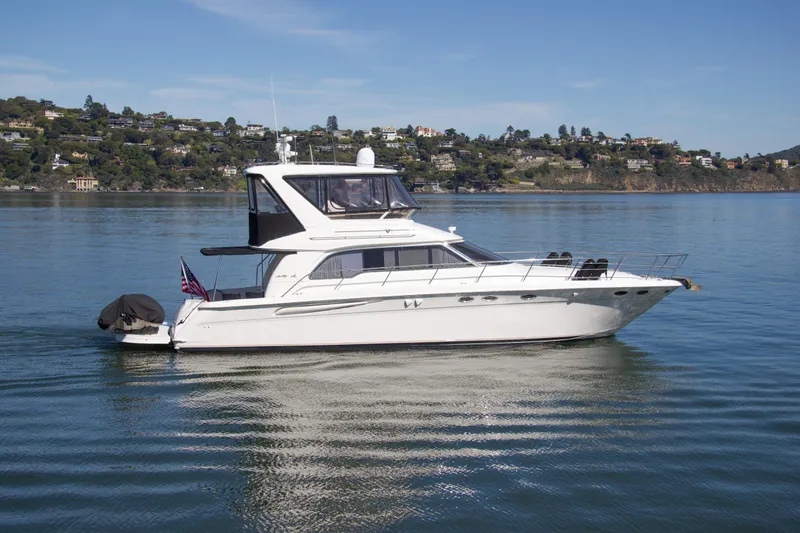 Slide: The Image of 1998 Sea Ray 480 Sedan Bridge yacht on calm water with scenic hillside background. - 3