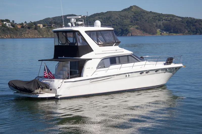 Slide: The Image of 1998 Sea Ray 480 Sedan Bridge yacht cruising on calm waters with scenic hills. - 4