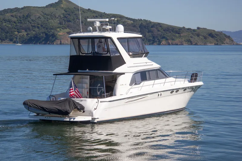 Slide: The Image of 1998 Sea Ray 480 Sedan Bridge yacht cruising on calm waters with scenic hills in background. - 5