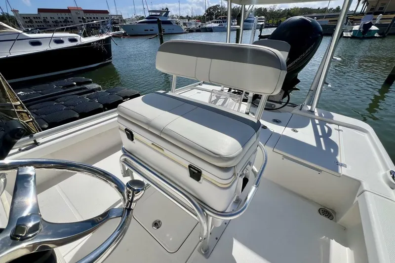 Slide: The Image of 2021 Mako 21 LTS boat interior with steering wheel and cushioned seating in marina. - 5