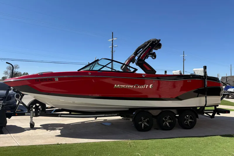Slide: The Image of 2022 MasterCraft X26 boat in red on a trailer, parked outdoors under clear blue sky. - 2