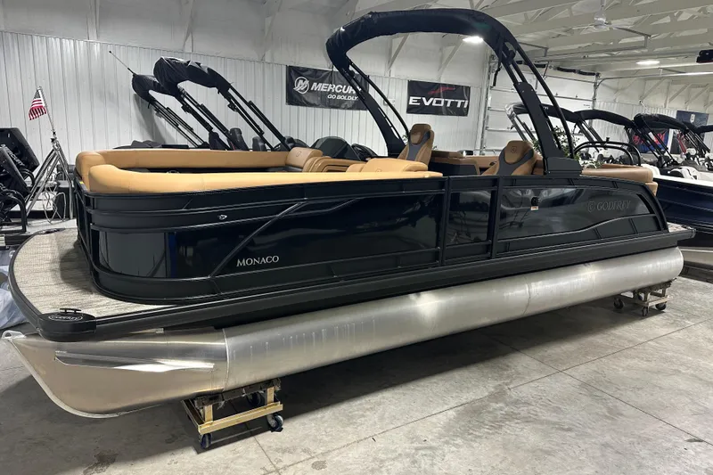 Slide: The Image of 2026 Godfrey Monaco 255 SB pontoon boat in showroom, featuring sleek black design and tan seating. - 4