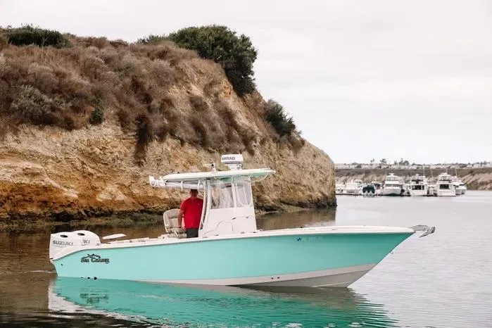 Slide: The Image of 2019 Carolina Skiff 27' Center Console boat on calm water near rocky shoreline. - 2