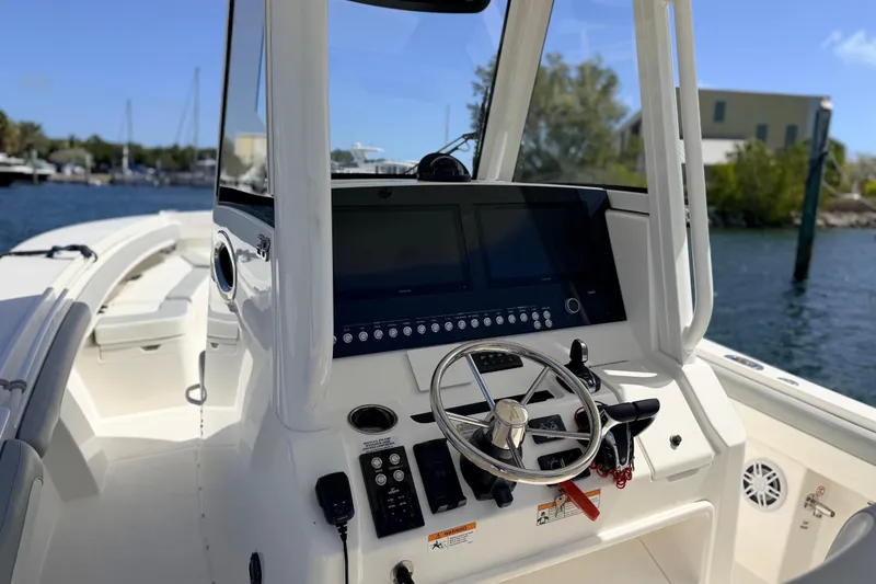Slide: The Image of 2022 Regulator 28 boat cockpit with steering wheel and control panel, docked by the water. - 10