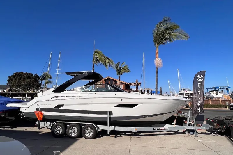 Slide: The Image of 2019 Cruisers Yachts 338 IO on trailer, displayed outdoors with palm trees and clear sky. - 2