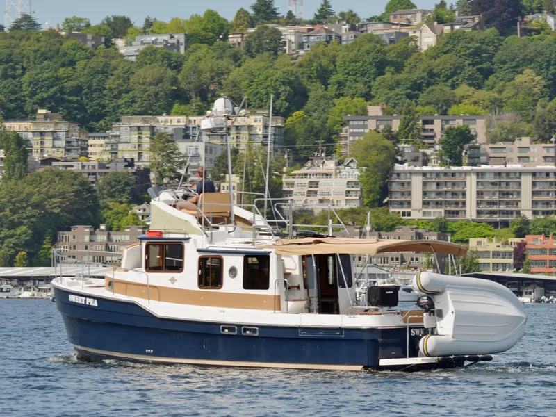Slide: The Image of 2013 Ranger Tugs R-31 CB boat cruising on a scenic waterfront with lush greenery and buildings. - 2
