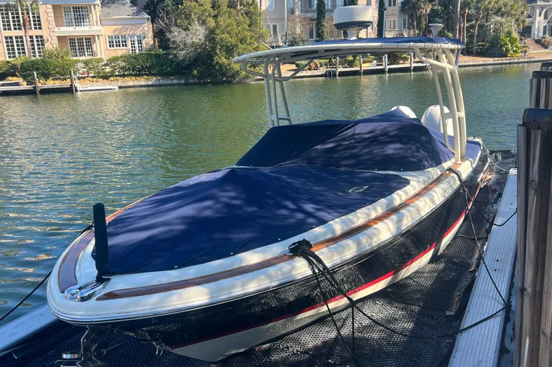 Slide: The Image of 2016 Chris-Craft Calypso 26 boat docked, covered with a blue tarp, in a scenic waterfront setting. - 47