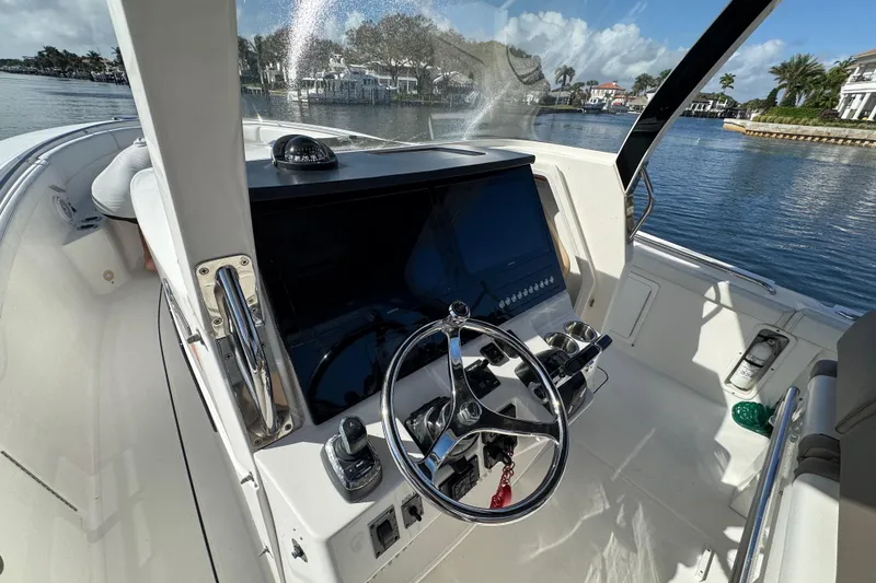 Slide: The Image of 2017 Edgewater 368CC boat helm with steering wheel and control panel, docked by waterfront homes. - 19