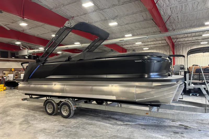 Slide: The Image of 2025 Manitou 24 Explore pontoon boat in a showroom, featuring sleek black design. - 7