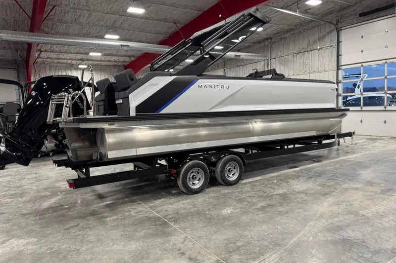 Slide: The Image of 2025 Manitou 24 Explorer pontoon boat on trailer in indoor showroom. - 3