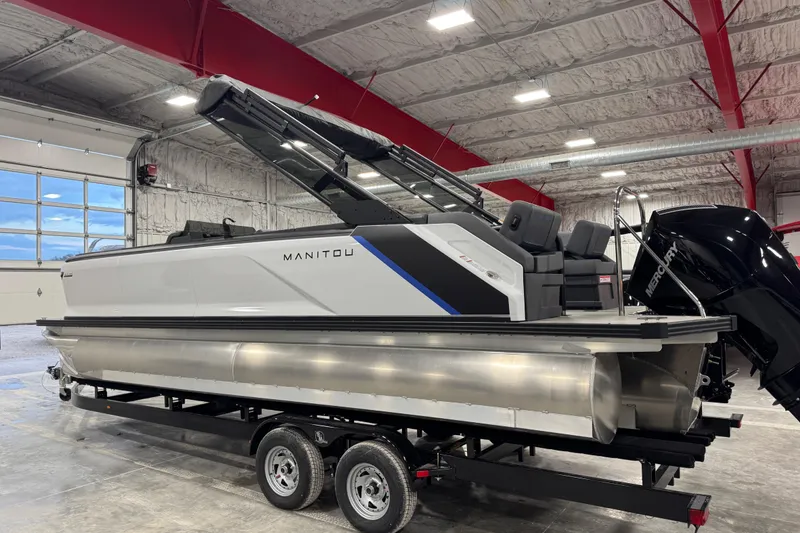 Slide: The Image of 2025 Manitou 24 Explorer pontoon boat in a warehouse, featuring sleek design and Mercury engine. - 4