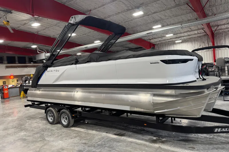 Slide: The Image of 2025 Manitou 24 Explorer pontoon boat on trailer in indoor showroom. - 5