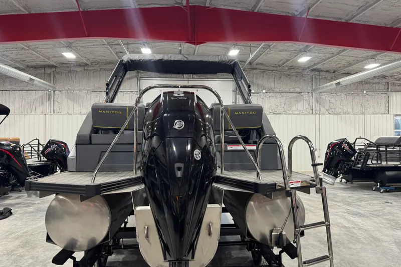 Slide: The Image of 2024 Manitou 24 Explorer pontoon boat in a showroom, featuring a sleek black motor. - 3