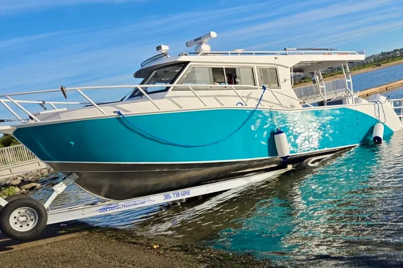 The Image of Custom Boat 34, 2025 model, turquoise hull, docked on a trailer by the water. - 0