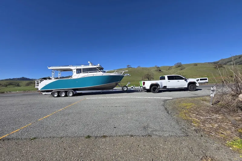 Slide: The Image of White truck towing a 2025 Custom Boat 34 on a trailer, scenic countryside background. - 2