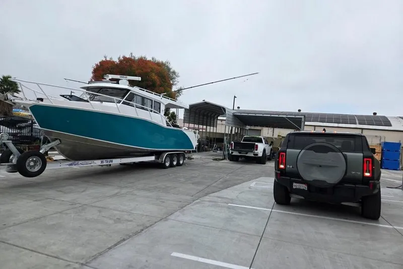 Slide: The Image of Custom Boat 34 (2025) on trailer, parked near vehicles in industrial area. - 3