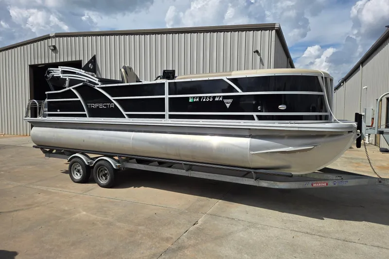 The Image of 2021 Trifecta SS 23C 2.75 pontoon boat on trailer, parked outside a warehouse. - 1