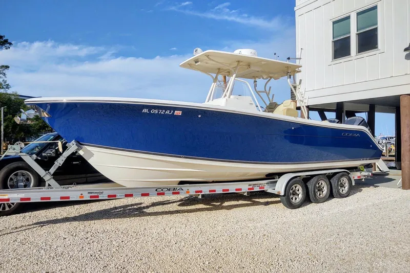 The Image of 2014 Cobia 296 Center Console boat on trailer, blue hull, parked near building. - 1