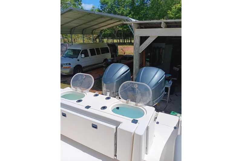 Slide: The Image of 2014 Cobia 296 Center Console with dual outboard engines and live wells, parked near a van. - 10
