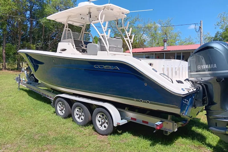 Slide: The Image of 2014 Cobia 296 Center Console boat on trailer with Yamaha engine, parked on grass. - 2
