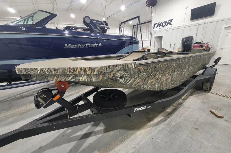 Slide: The Image of 2026 Thor 1860 Timber Hammer Elite boat with camouflage design on trailer in showroom. - 3