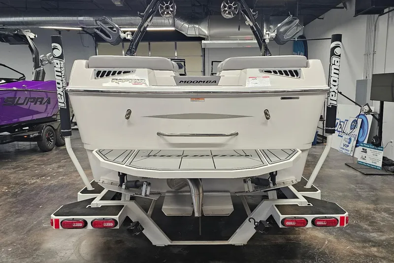 Slide: The Image of 2024 Moomba Mojo boat rear view in showroom, featuring swim platform and trailer. - 9