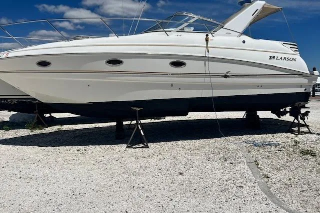 Slide: The Image of 2004 Larson 330 boat on stands, white hull, clear sky background. - 2