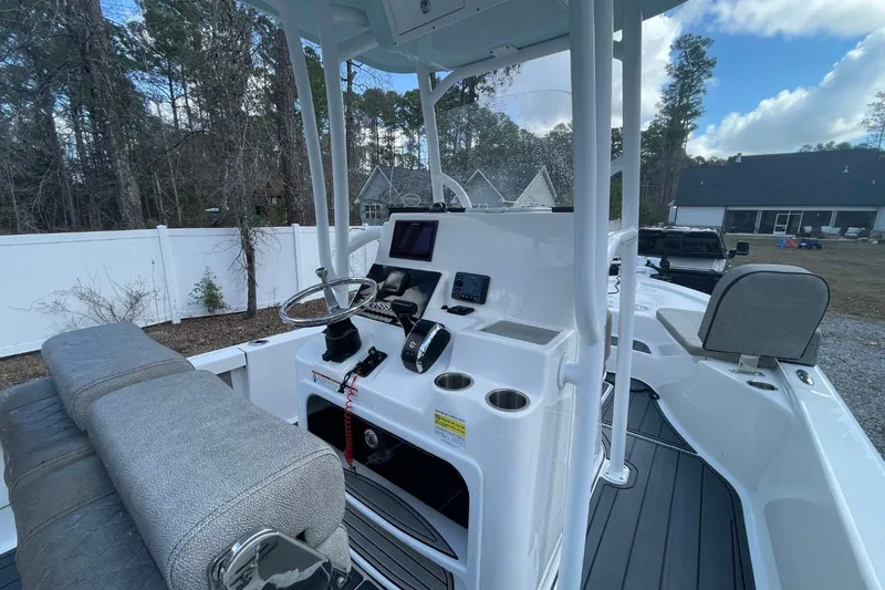 Slide: The Image of 2023 Sea Pro 248 Bay boat interior with steering console and seating, surrounded by trees and houses. - 7