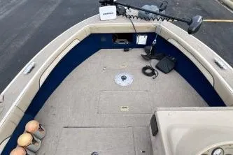 Slide: The Image of 1999 Sylvan 1700 boat interior with beige and blue seating, fishing equipment, and a trolling motor. - 8