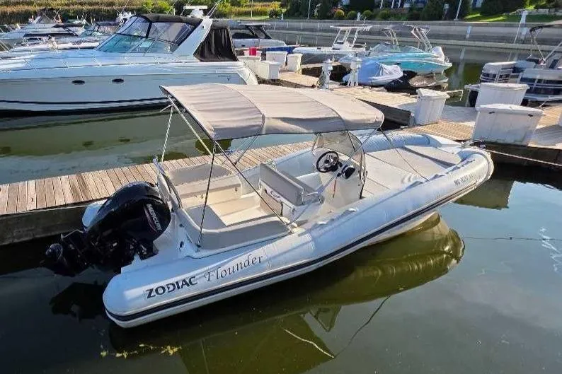 Slide: The Image of 2024 Zodiac N-ZO 680 boat docked in marina, featuring canopy and outboard motor. - 13
