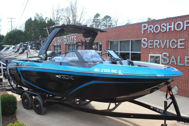 The Image of 2023 Tigé 23ZX boat in blue and black on trailer outside dealership. - 1