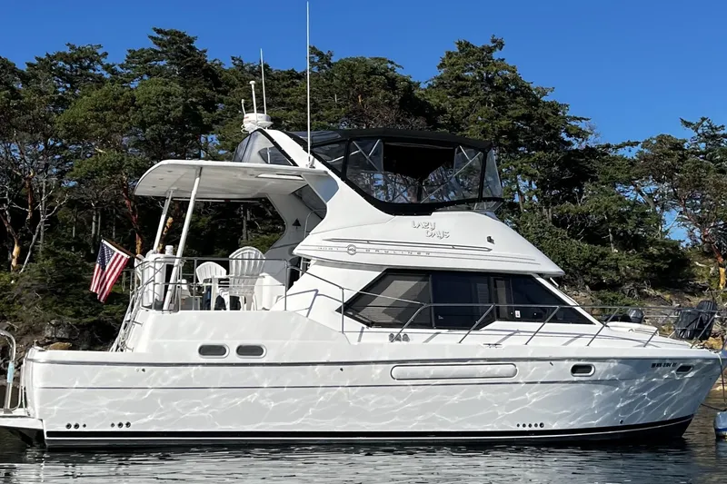 The Image of 1996 Bayliner 4087 Aft Cabin Motoryacht on calm water, surrounded by trees. - 0